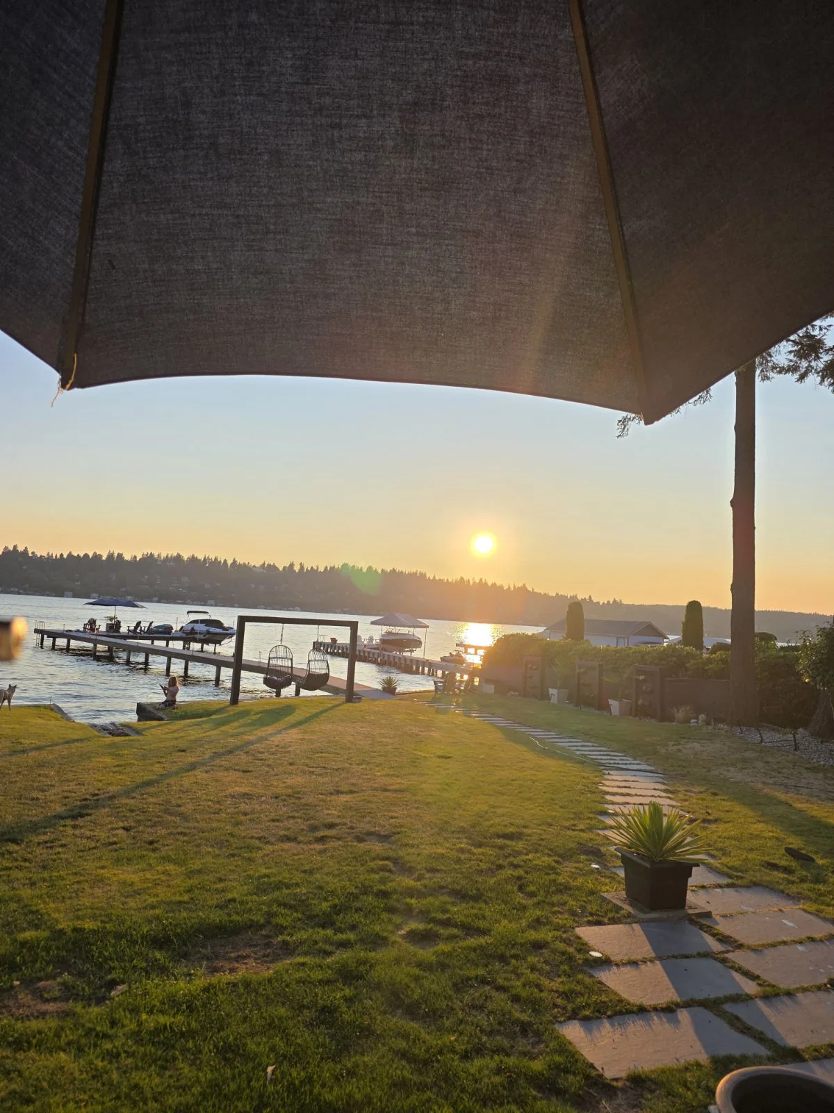 Sunset over a lakeside yard with a dock, boats, and outdoor seating.
